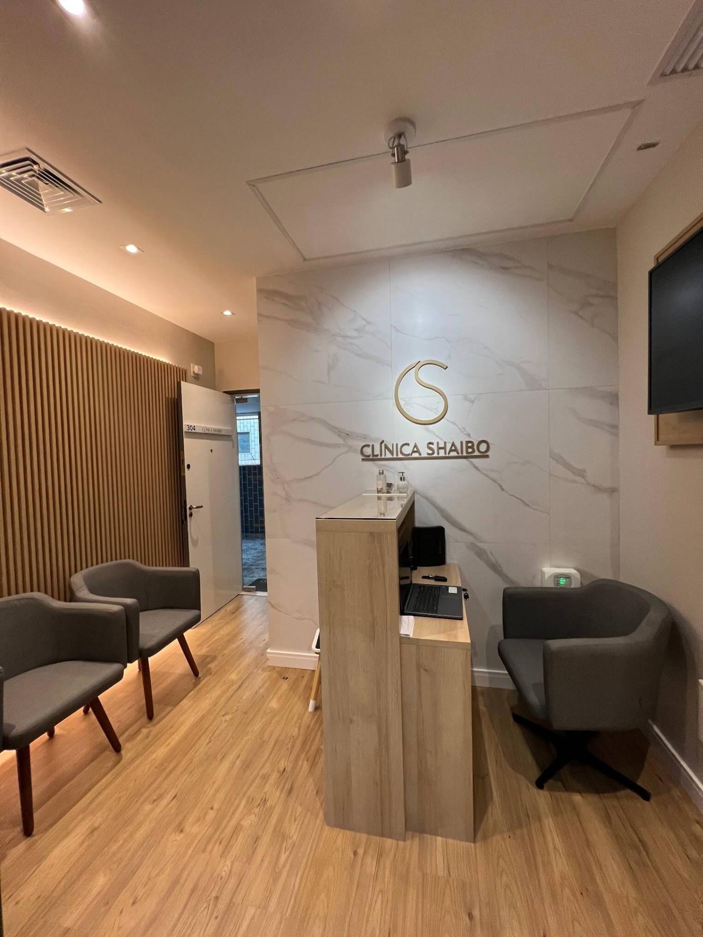 Recepção da Clínica Shaibo na Ilha do Governador com parede em mármore e logotipo dourado